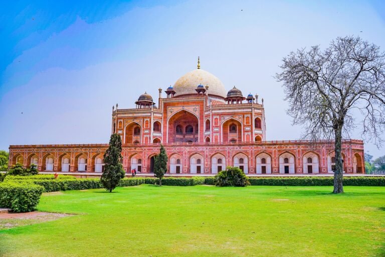 The red sandstone and white marble structure of Humayun's Tomb stands prominently behind a manicured green lawn under a clear blue sky.